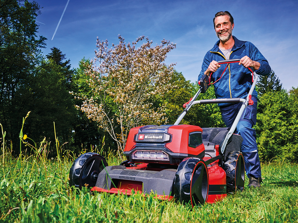 A man mowing the garden with a electric lawn mower. 