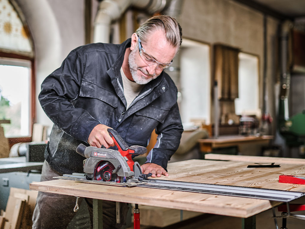 A man using the handheld circular saw in a workshop.