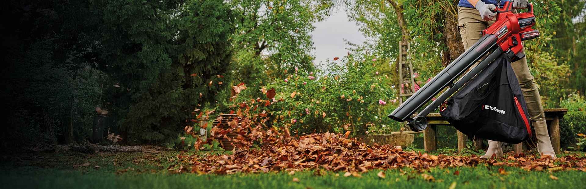 A person vacuums autumn leaves in the garden using an Einhell leaf vacuum.