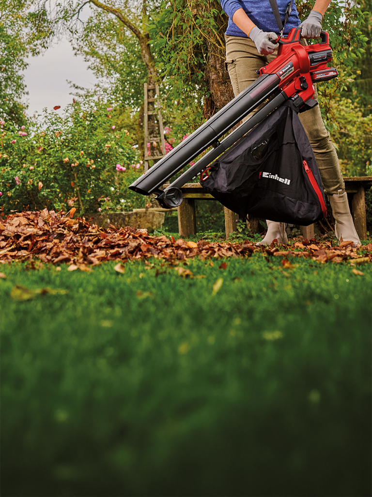 A person vacuums autumn leaves in the garden using an Einhell leaf vacuum.