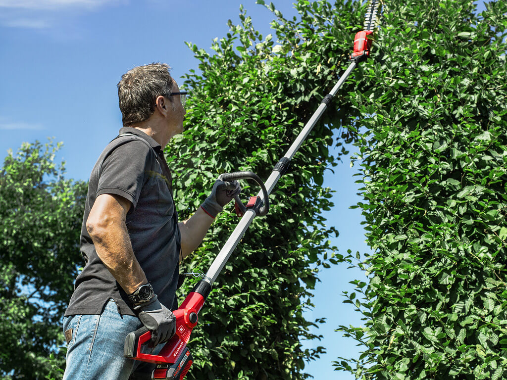 A man cuts the hedge with an Einhell cordless telescopic hedge trimmers
