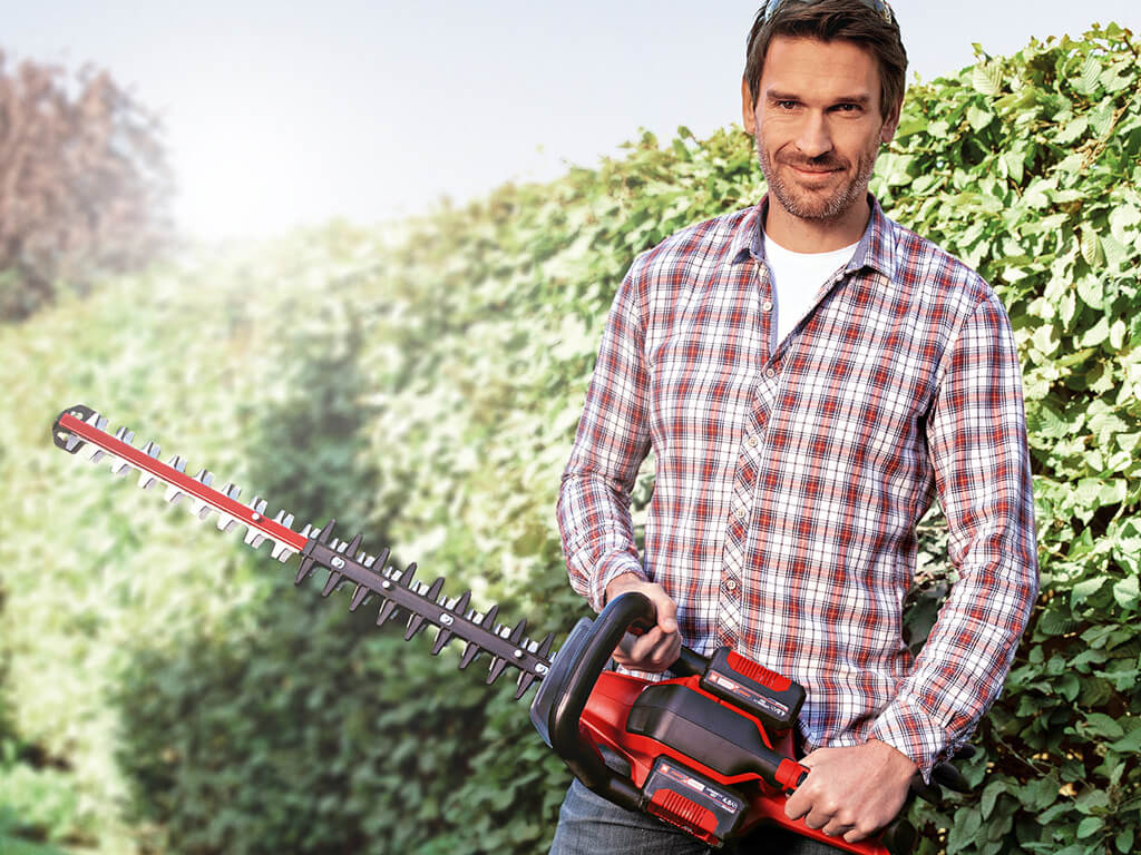 A man cuts the hedge with an Einhell cordless fence saw