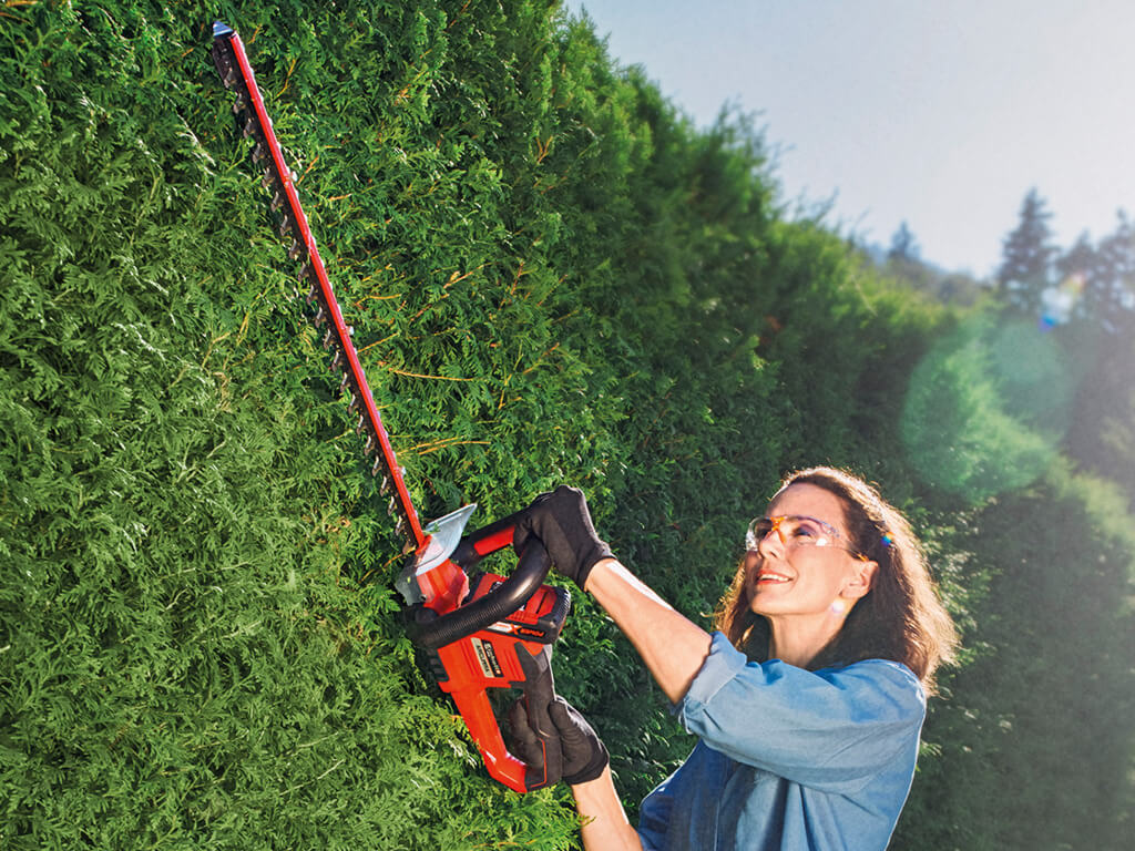 A woman cuts the hedge with an Einhell cordless fence saw