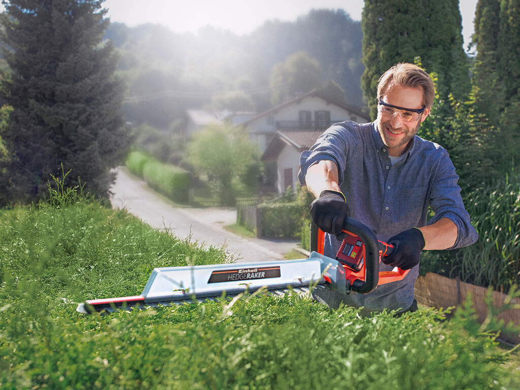A man cuts the hedge with an Einhell cordless fence saw
