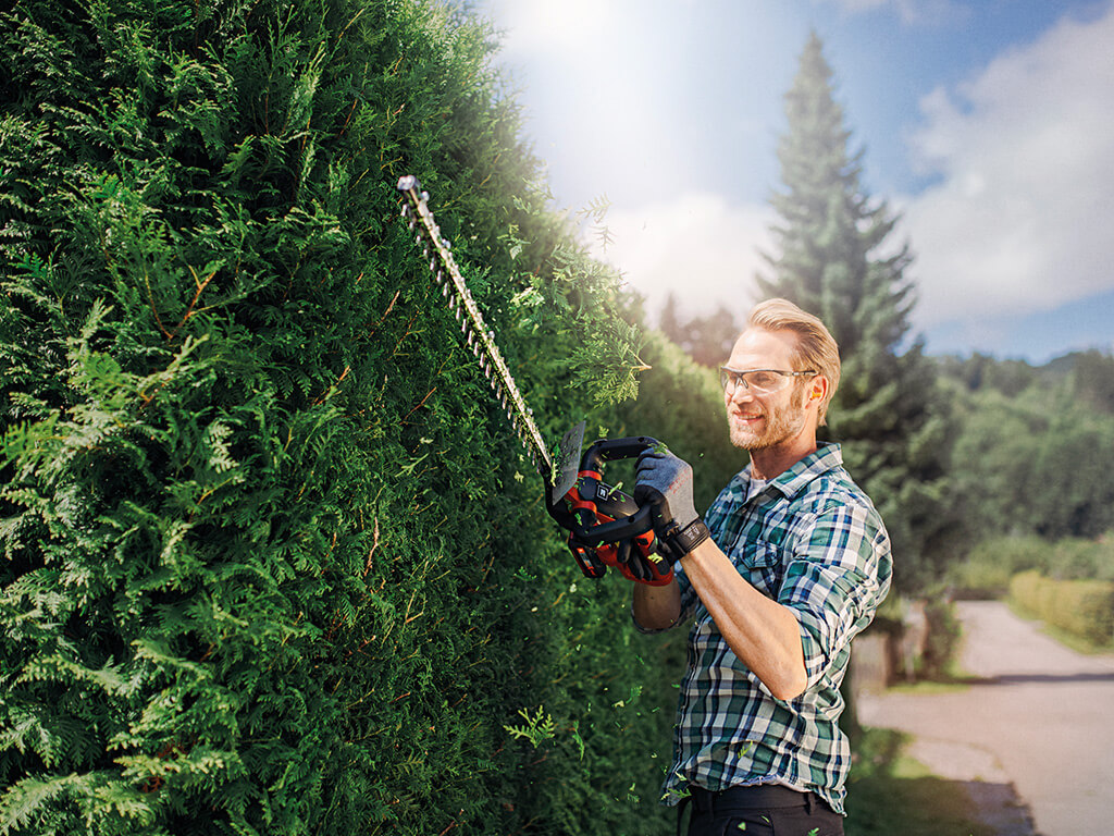 A man cuts the hedge with an Einhell cordless fence saw