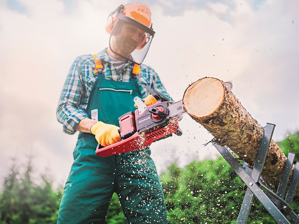 A man using a cordless chainsaw to chop off a piece of a tree trunk.