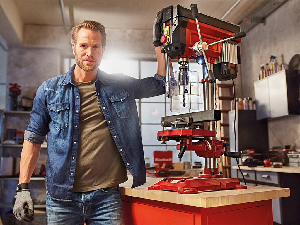 A man standing next to the bench drill.
