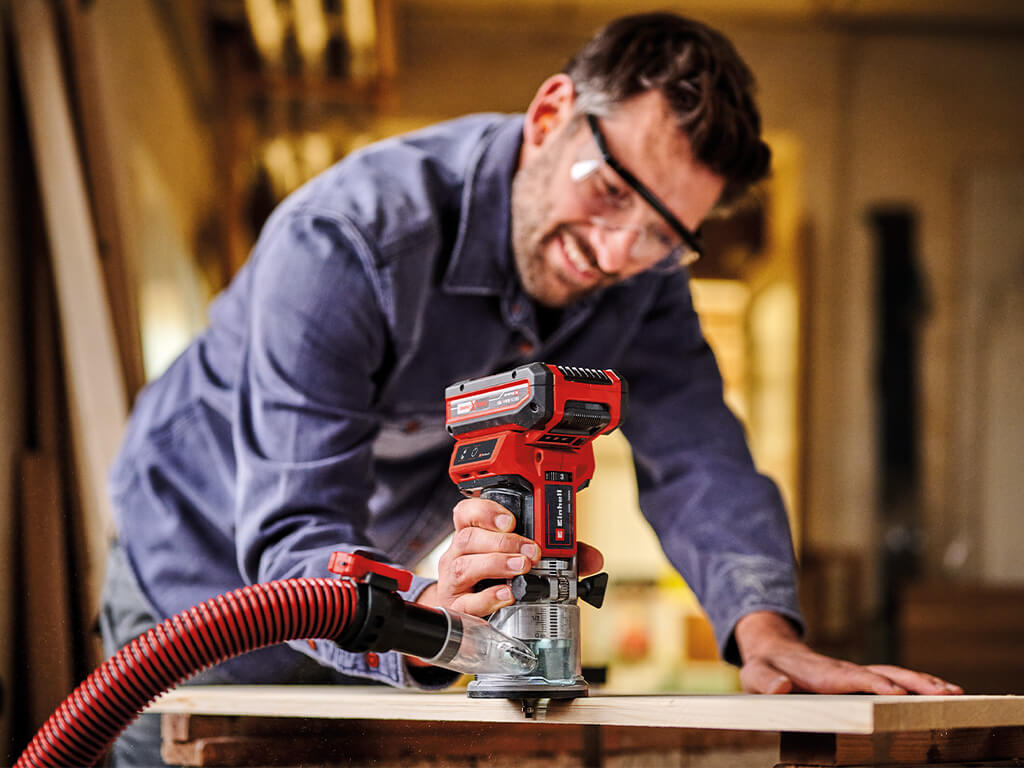 A man routing the edge of a wooden panel with the Einhell battery-powered edge router TP-ET 18 Li BL
