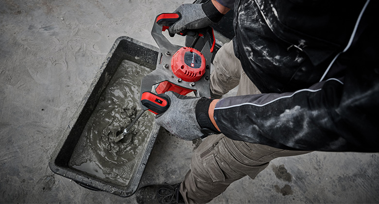 A person stirs cement mixture in a rectangular container with a mixing tool.