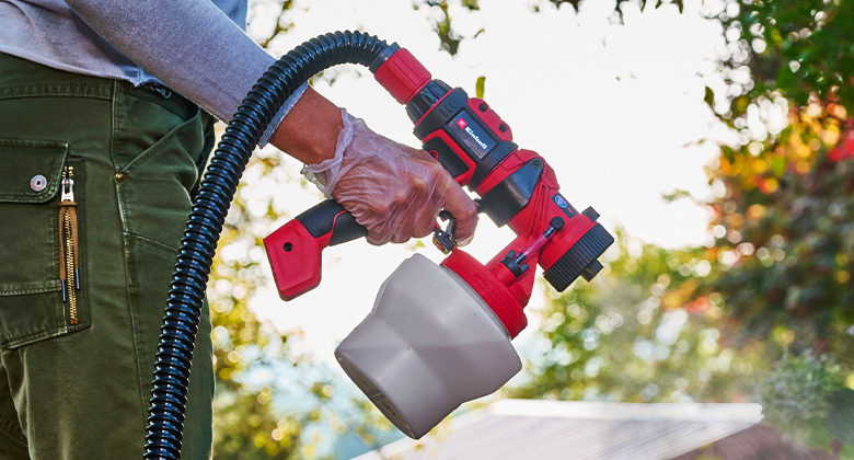 Close-up of a hand holding a paint sprayer with a red handle.