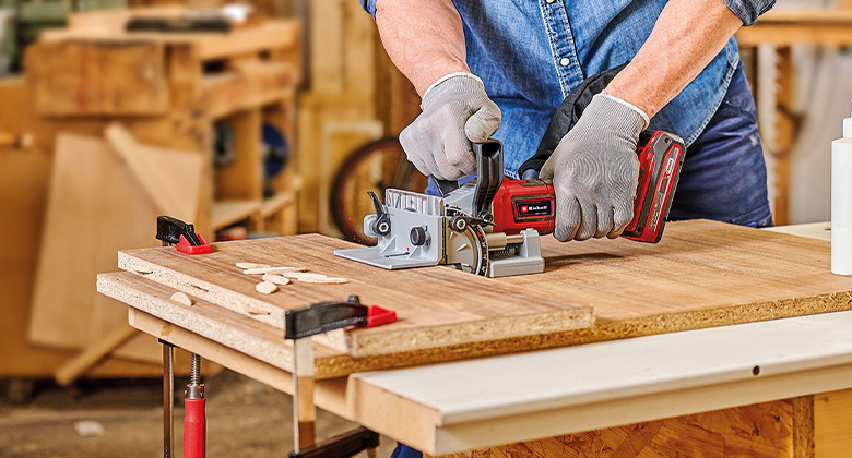 A cordless biscuit jointer is being used to cut precise slots for biscuits in wooden boards.