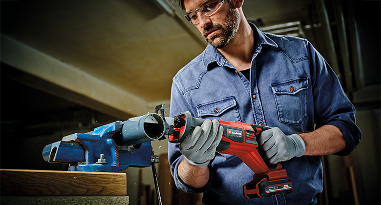 Man using a cordless Einhell reciprocating saw to cut a pipe.