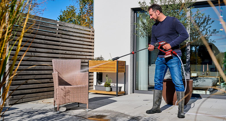 a man is cleaning an outdoor chair with the Einhell HYPRESSO
