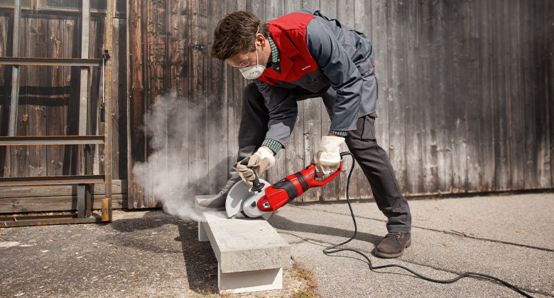 A craftsman cutting a concrete block with a corded angle grinder.
