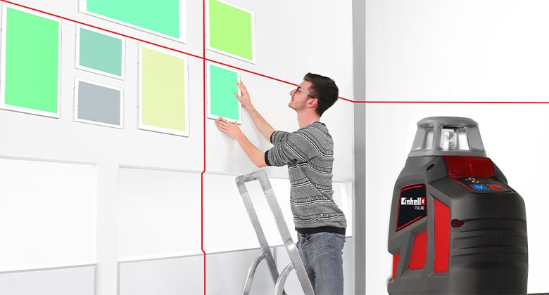 man hanging pictures with a cross laser