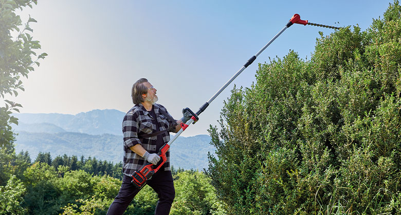 A man is trimming a hedge with an Einhell cordless multifunctional tool