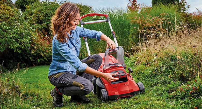 A woman plugging a Power X-Change battery into her cordless lawnmower.