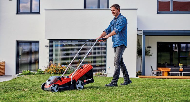 A man mowing a small lawn in front of his house with a cordless lawnmower.