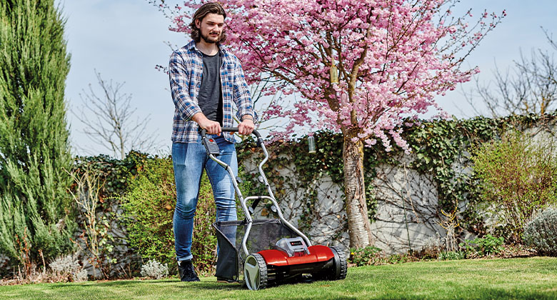 A man using the hand lawn mower in his garden. 