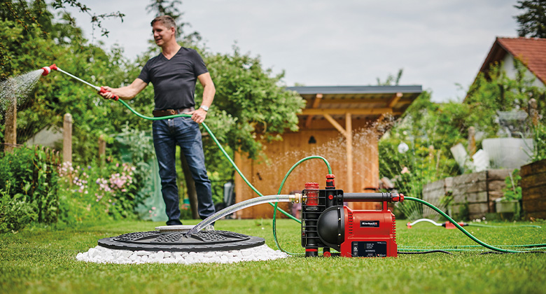 A man watering the plants in his garden with a garden water pump.