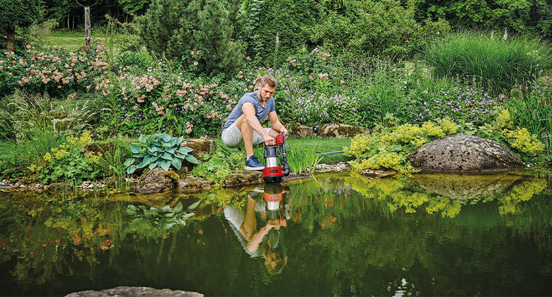 A man placing a garden water pump in a pond. 