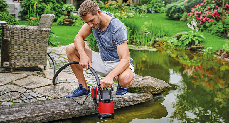 A man placing a garden water pump into a small pond. 