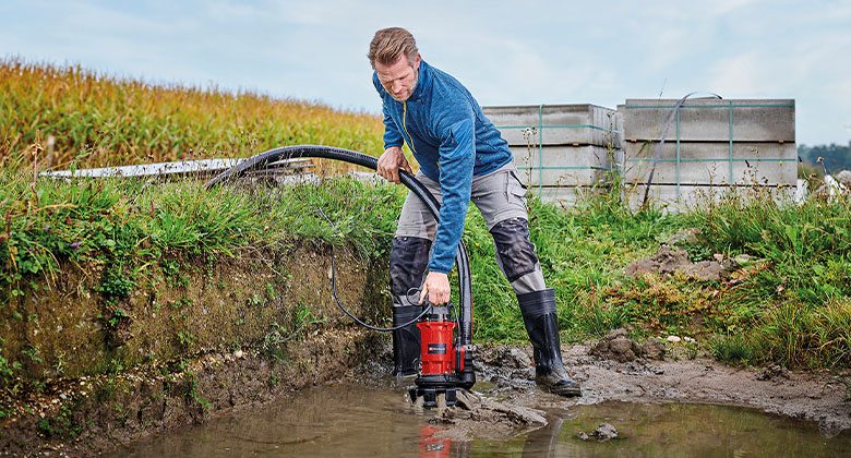 A man pulling out the dirt water pump out of the the mud.