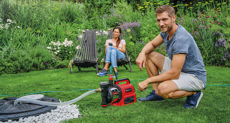A man kneeling next to a garden water pump. 