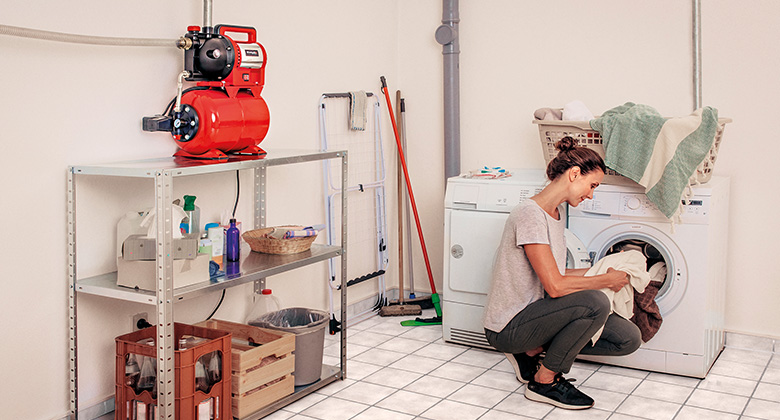 A woman sitting in a washing room next to a garden water pump.
