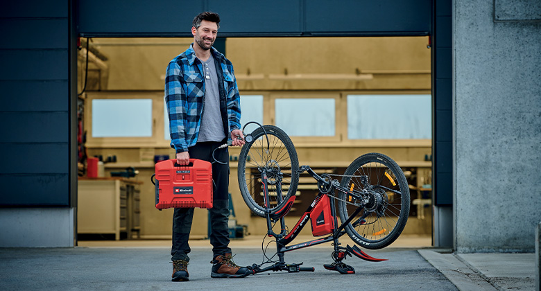 man is standing next to a bicycle; he is holding a portable compressor